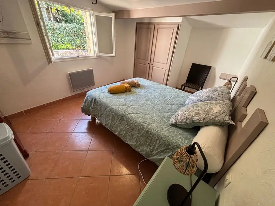 Chambre cosy avec lit double, fenêtre ouverte et décoration chaleureuse, dans une maison de vacances en Corse.