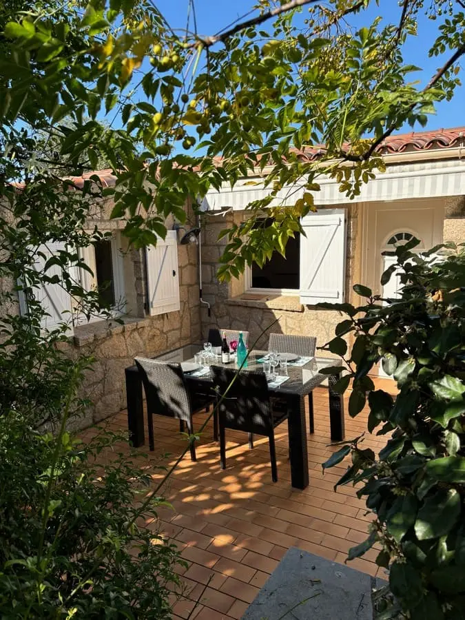 Cour aménagée d'une maison en Corse avec une table en plein air entourée de végétation.