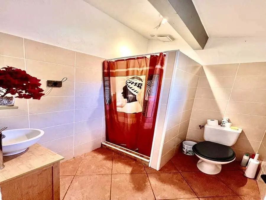 Salle de bain avec douche, rideau rouge, lavabo moderne et toilettes, maison de vacances en Corse.