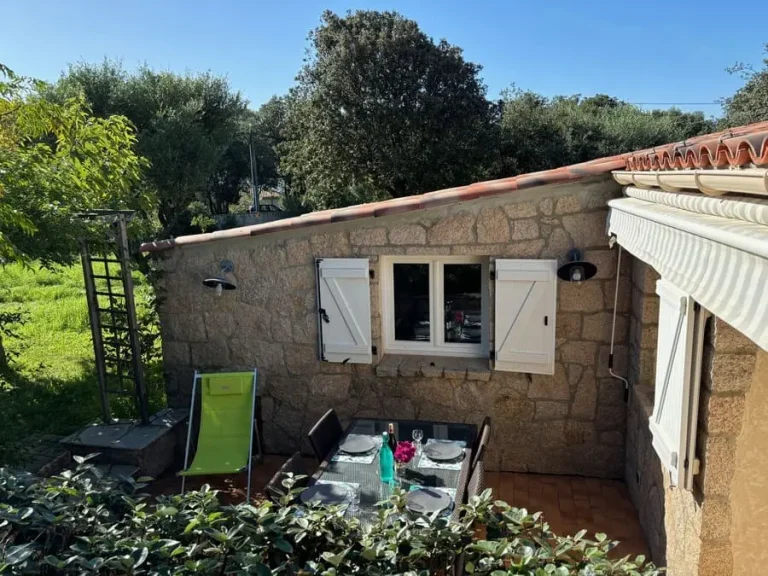 Terrasse extérieure aménagée avec table dressée et chaises, entourée de verdure dans une maison en pierre en Corse.