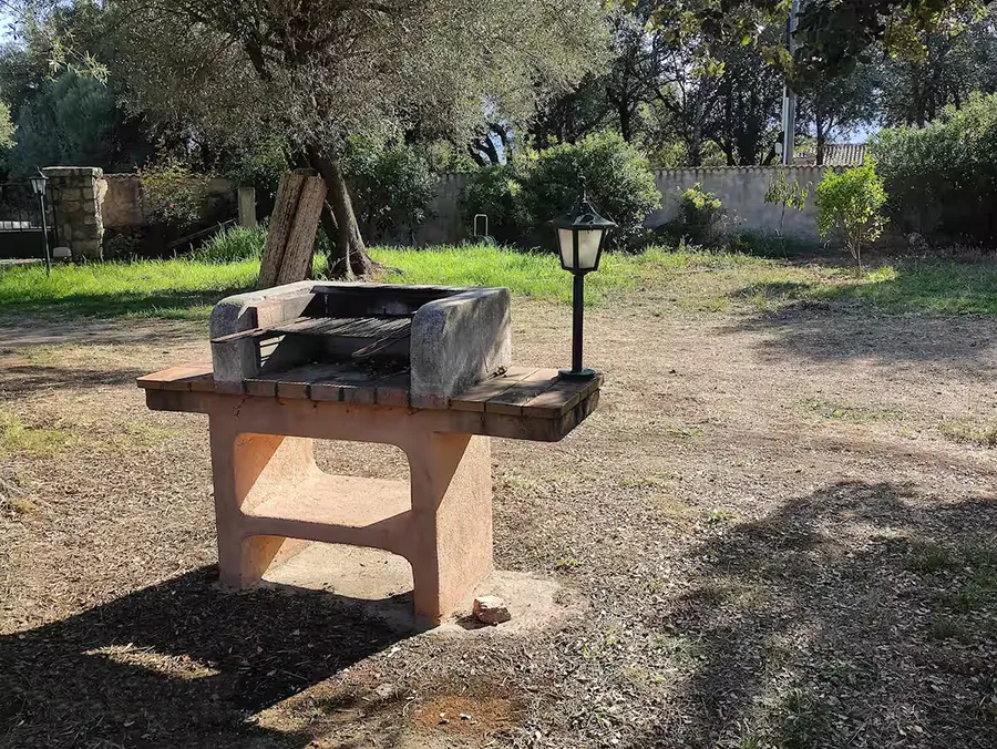 Barbecue extérieur en pierre de la villa Caseddu Jardin et Mer, dans un jardin verdoyant et ensoleillé, idéal pour des repas conviviaux lors de vos vacances en Corse du Sud.