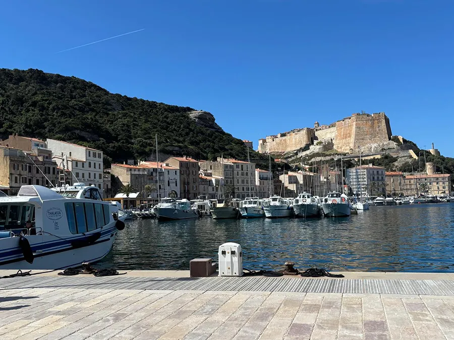Quai du port de Bonifacio, Corse du Sud, avec bateaux, citadelle perchée et bâtiments colorés, pour vacances nautiques.