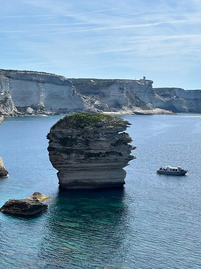 Rocher emblématique en mer à Bonifacio, Corse du Sud, avec falaises et bateau, pour vacances exceptionnelles.