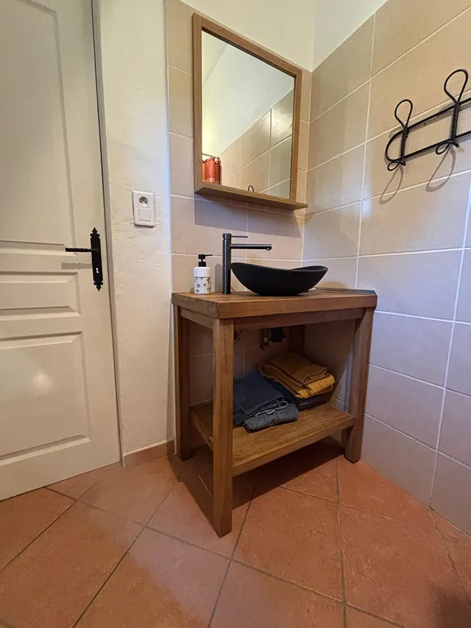 Salle de bain moderne de la villa Caseddu Jardin et Mer avec vasque noire sur meuble en bois clair, miroir et carrelage beige, offrant confort pour votre location de vacances en Corse du Sud.